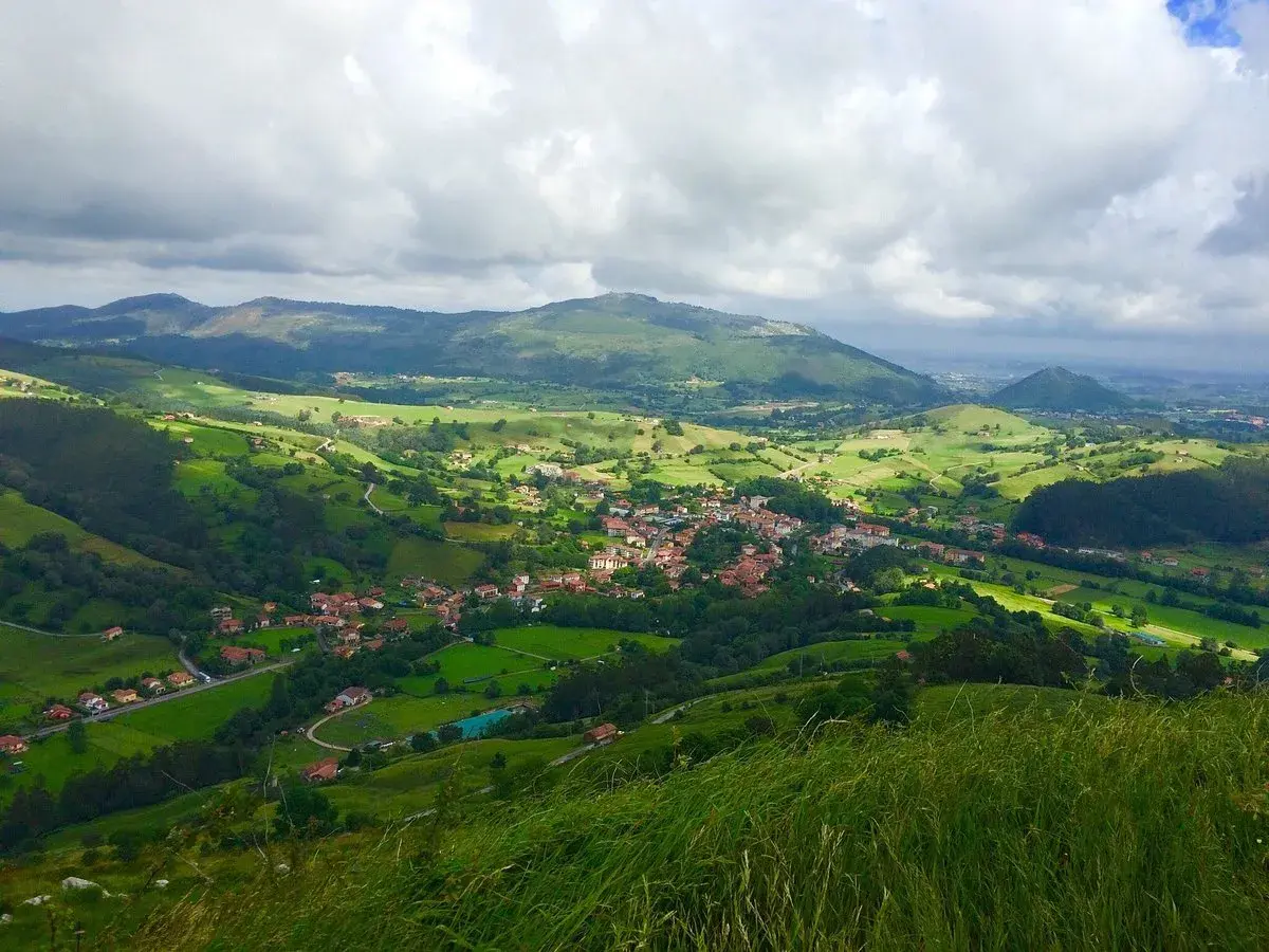 Paisaje verde y montañoso, con un pueblo en el valle. La **ruta Tetas de Liérganes** ofrece vistas espectaculares.