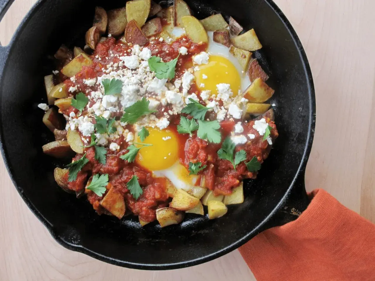 Plat savoureux : recette pomme de terre oeuf avec sauce tomate, fromage émietté et persil frais, servi dans une poêle en fonte.