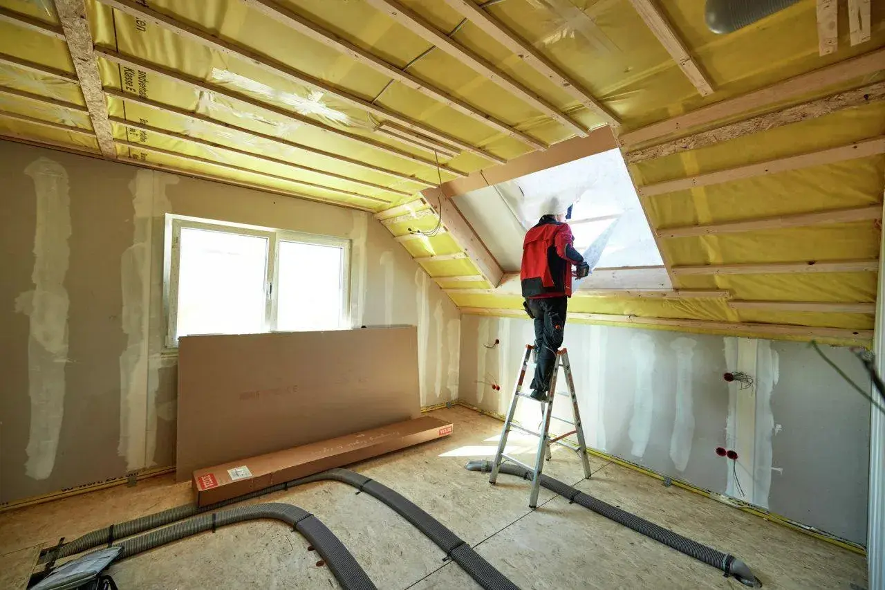 Lavoratore su scala installa isolamento giallo nel sottotetto, una scelta chiave per capire se meglio isolare il tetto o il sottotetto.