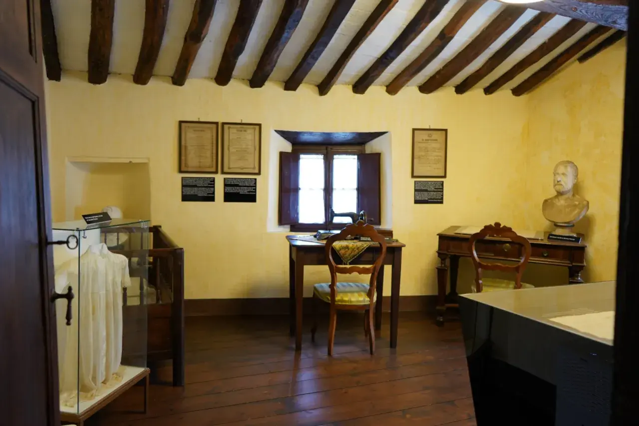 Interno di una casa museo, con travi a vista, una scrivania con macchina da cucire, un busto e un abito in esposizione. Un luogo dove le case della memoria prendono vita.
