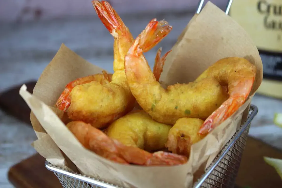 Crujientes gambas a la gabardina doradas, servidas en una cesta metálica con papel marrón.