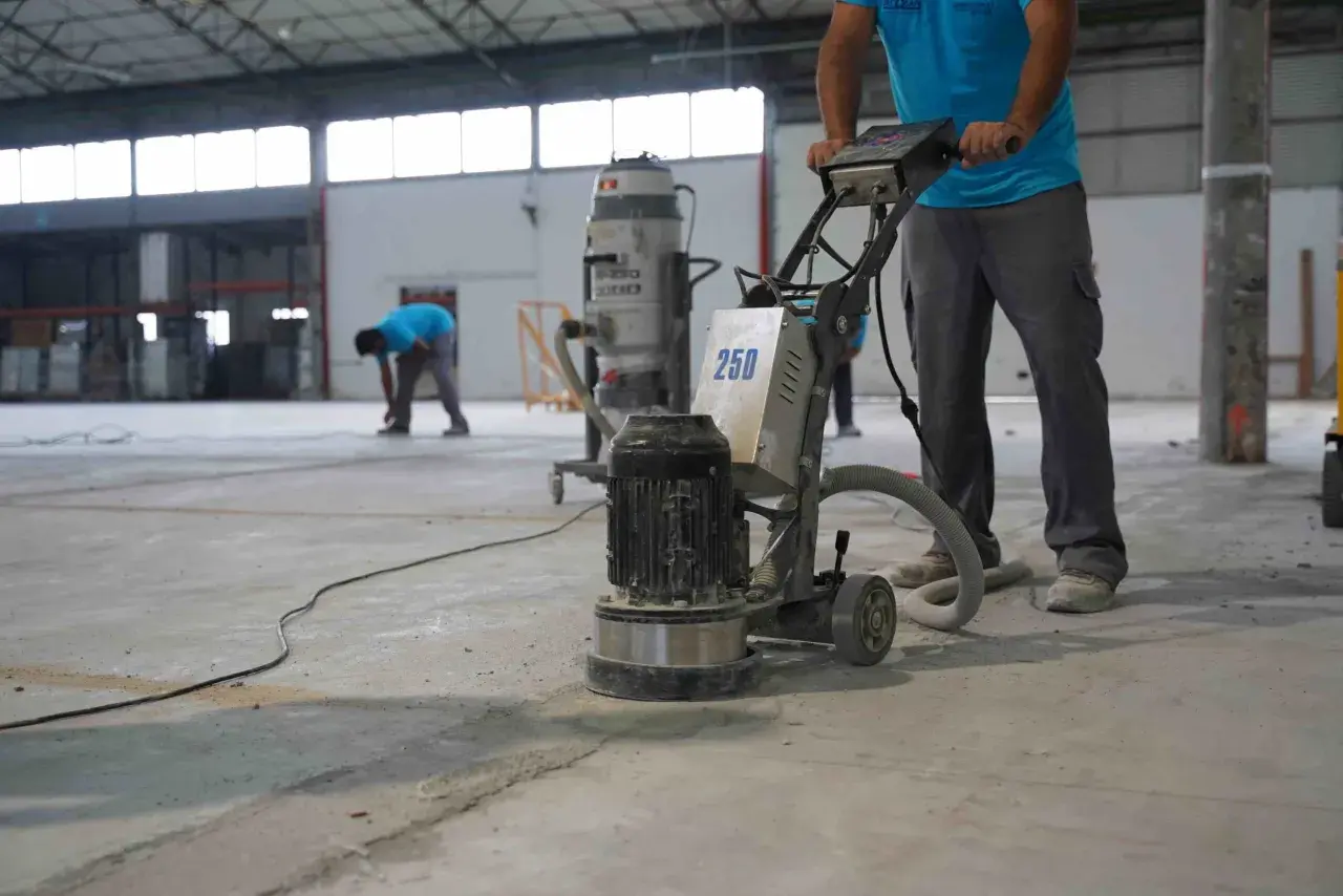 Trabajadores pulen un suelo de hormigón con una máquina. Se muestra cómo hacer hormigón para suelo, preparando la superficie.