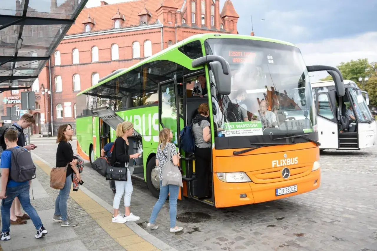 Pomarańczowo-zielony autobus FlixBus na przystanku, pasażerowie wsiadają.