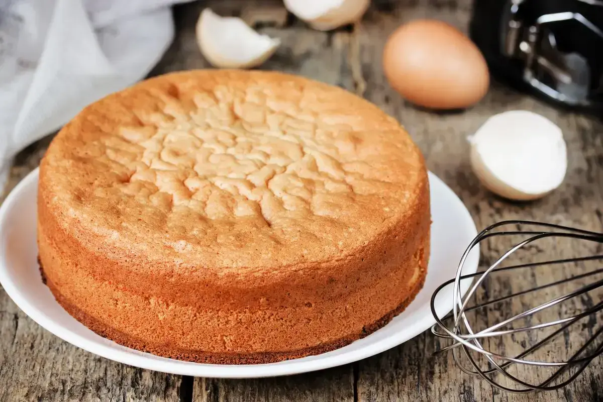 Torta 12 cucchiai soffice e dorata, pronta per essere decorata. Ingredienti per la torta 12 cucchiai sparsi sul tavolo: uova, frusta.