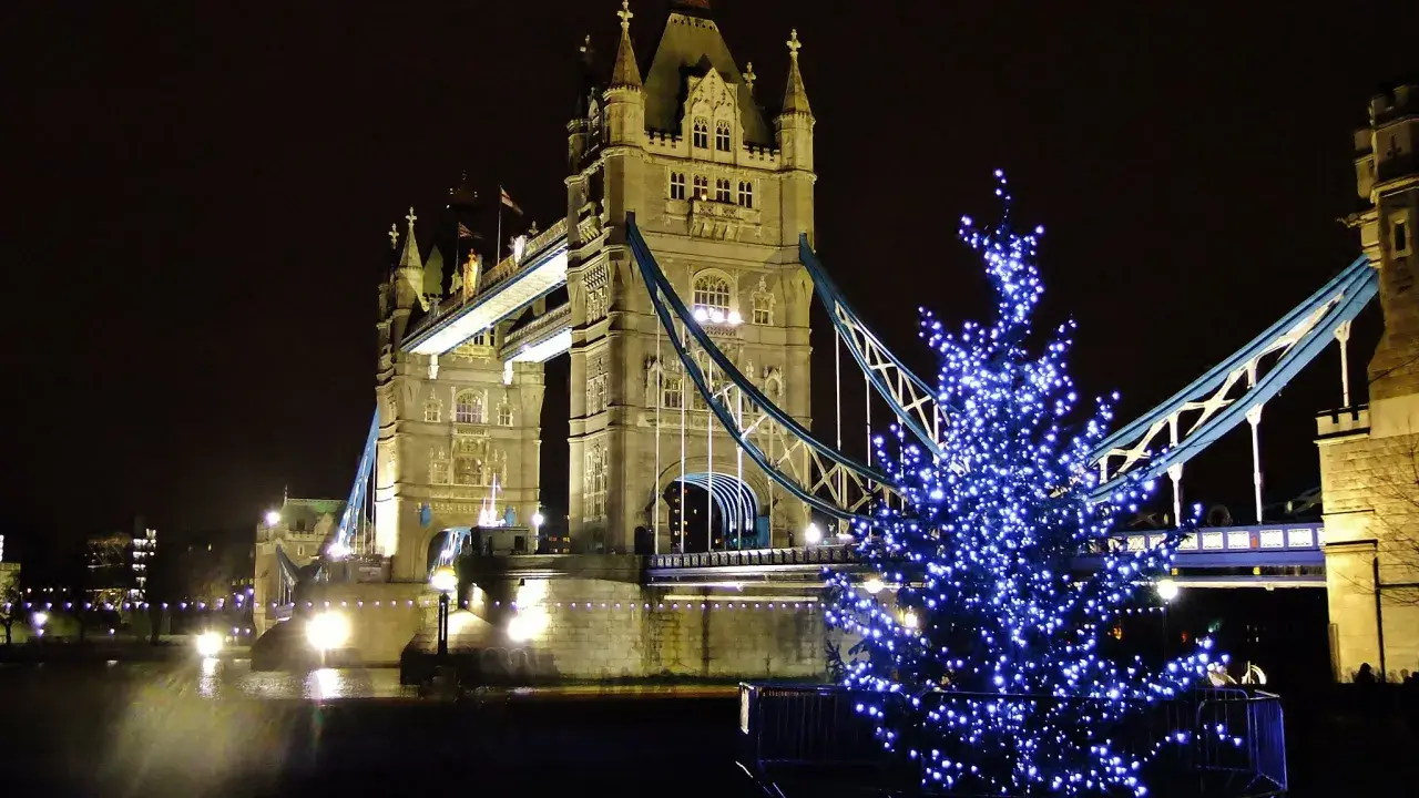 Albero di Natale illuminato con luci blu davanti al Tower Bridge di Londra, evocando l'atmosfera dei mercatini di Natale in inglese.