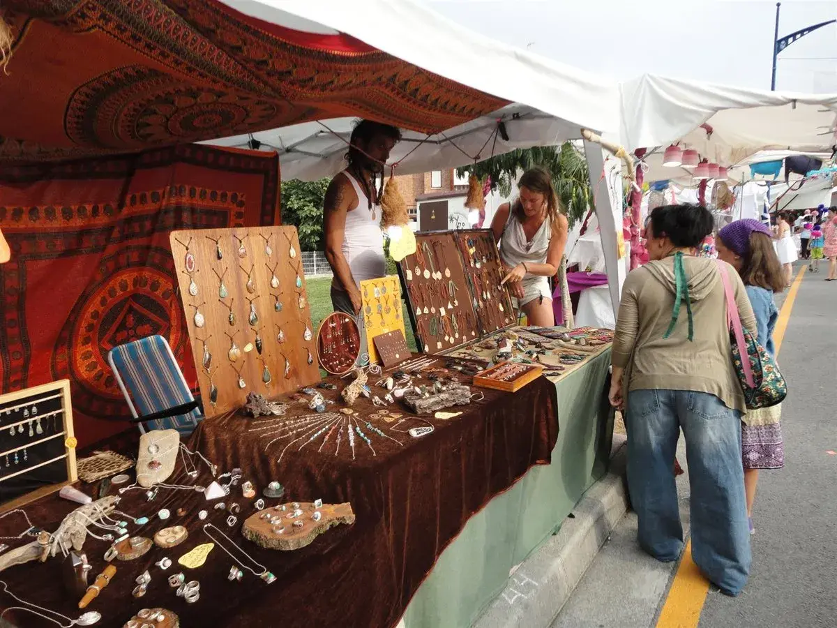 En el **mercado hippie Argaños**, se exhiben collares y pulseras artesanales. Una vendedora muestra su mercancía a dos clientas.