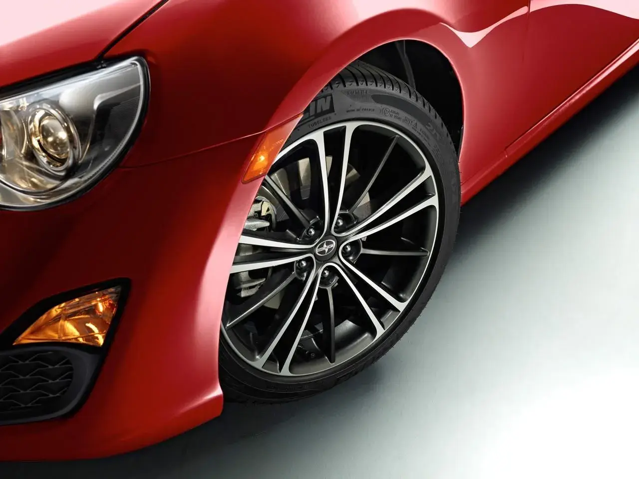 Część czerwonego samochodu Scion FR-S z reflektorem i felgą.