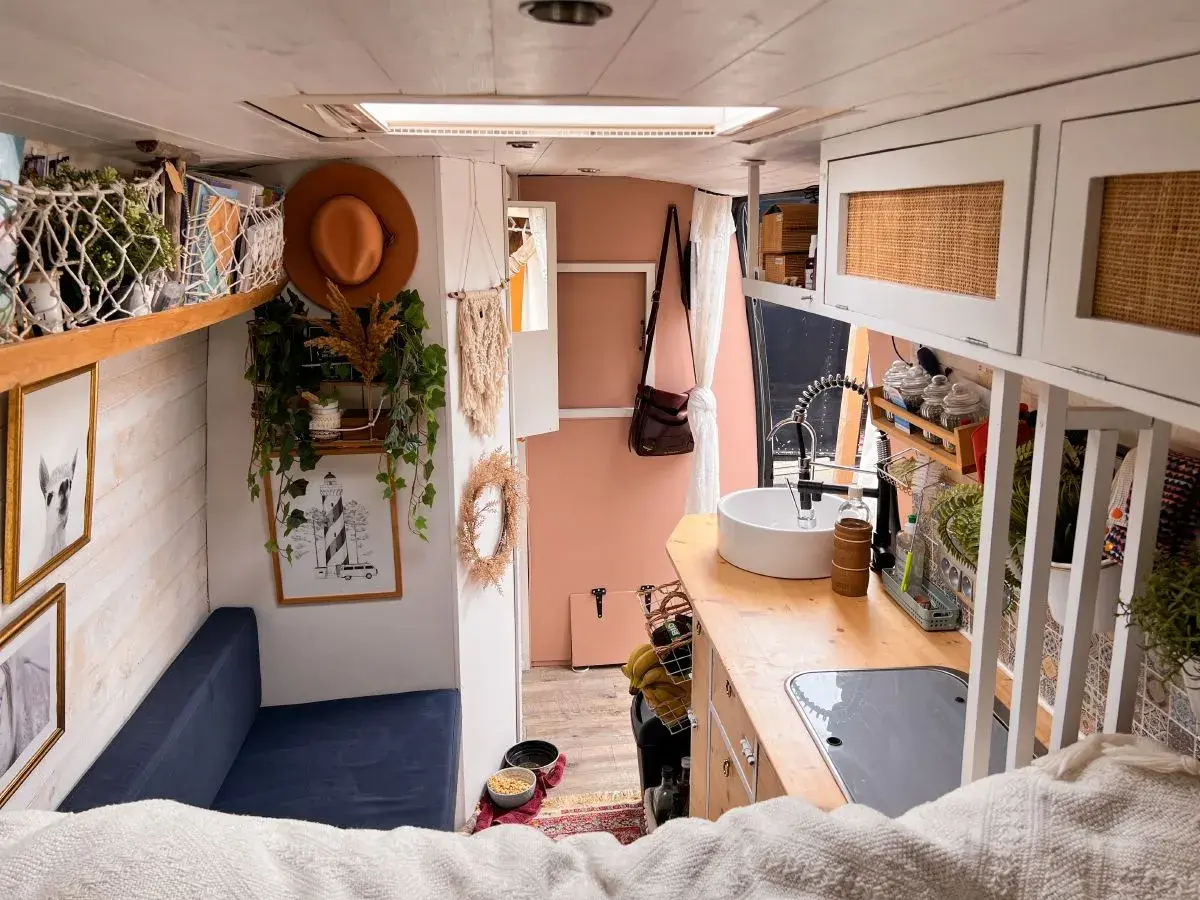 Ambiance chaleureuse et bohème pour ce deco interieur van. Un canapé bleu, des plantes grimpantes, un chapeau tendance et une cuisine fonctionnelle.