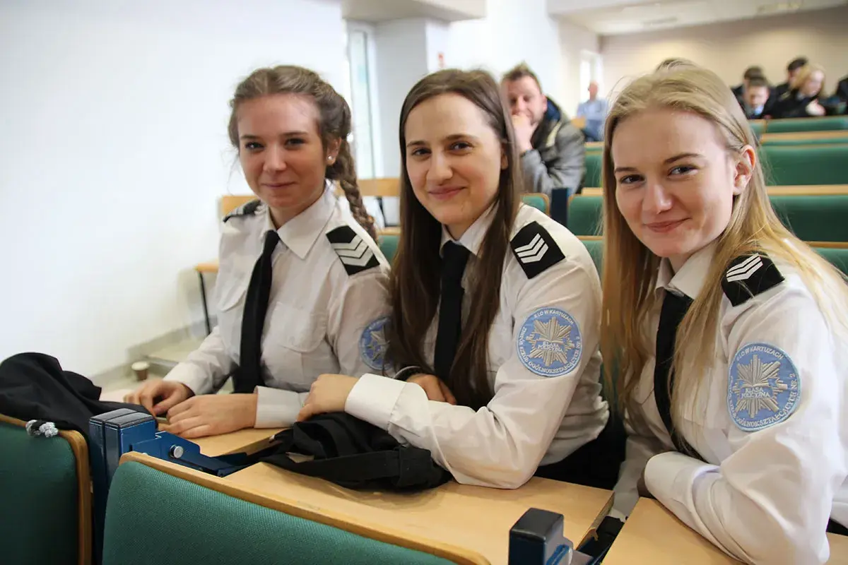 Trzy uśmiechnięte studentki w mundurach policyjnych siedzą w sali wykładowej. To przyszłość policji, ich studia policyjne dopiero się zaczynają.