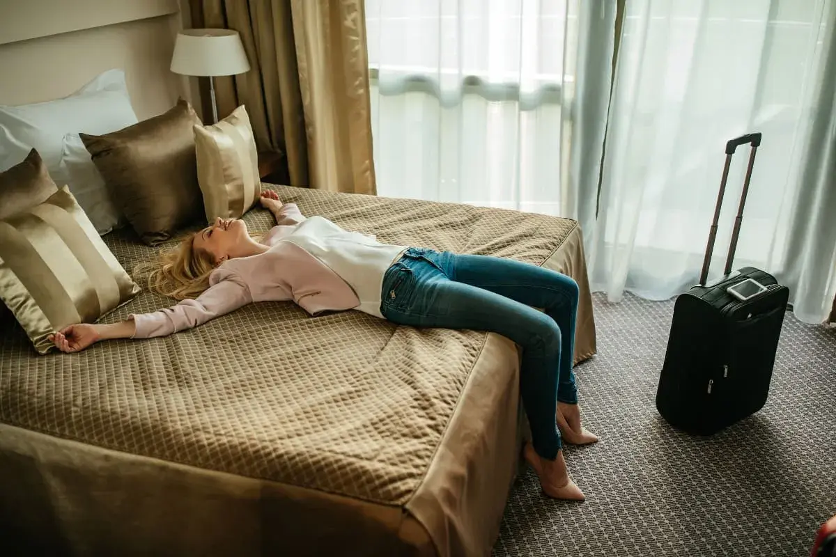 Zmęczona podróżą kobieta odpoczywa na łóżku w hotelu. Szukasz noclegów w Polsce? Sprawdź oferty!