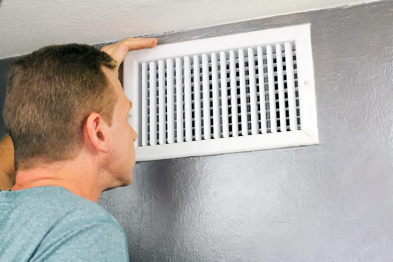 Hombre revisa un conducto de ventilación, mostrando diferentes tipos de rejillas para el aire acondicionado.