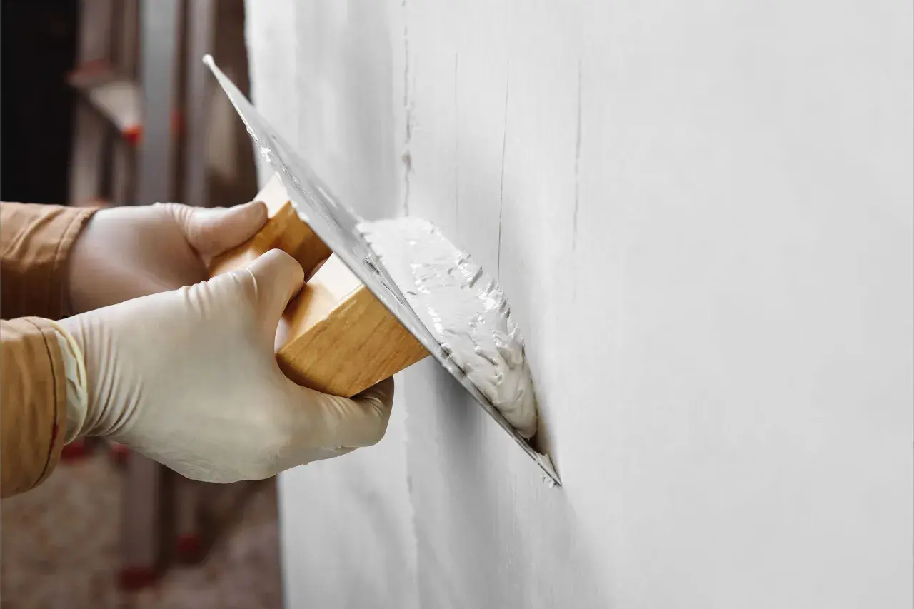 Manos con guantes aplican yeso a una pared. Pregúntate: cuanto tarda el yeso en secar para poder pintar.