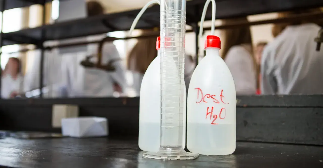 Bouteilles d'eau distillée et éprouvette graduée sur un établi de laboratoire, prêtes pour la stérilisation eau chaude.