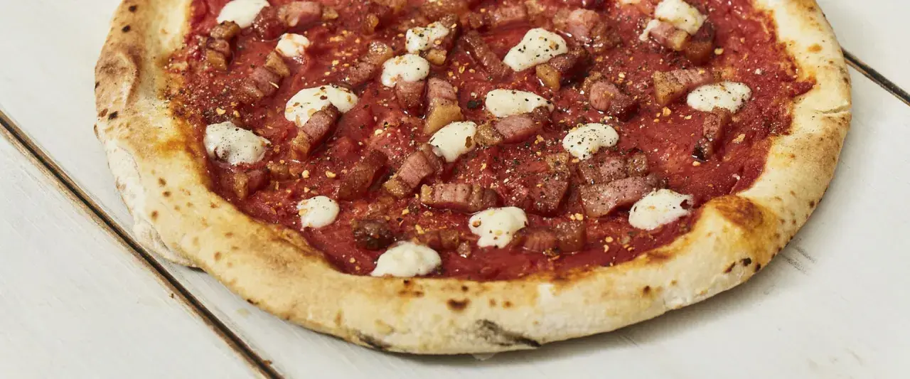 Pizza con guanciale croccante, pomodoro e fiocchi di pecorino, un sapore intenso e autentico.