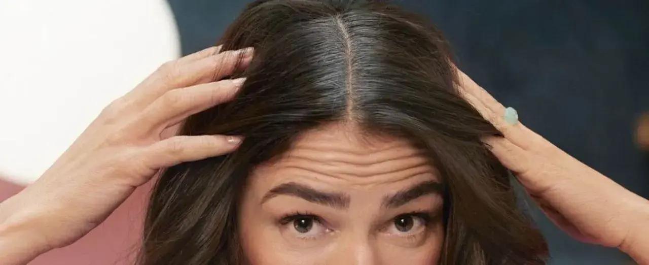 Mujer revisa su cabello oscuro con algunas canas. ¿Buscas como eliminar las canas para siempre?