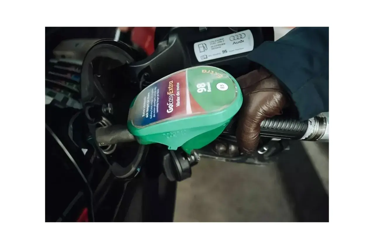 En hand med brun handske håller i en bensinpump med etiketten "GoEasyExtra 98 Bensin E5".