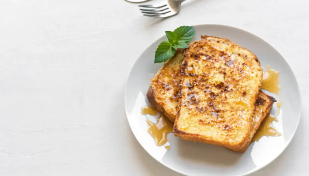 Dos rebanadas de tostada francesa dorada, bañadas en sirope y decoradas con menta. Una deliciosa french toast receta para el desayuno.