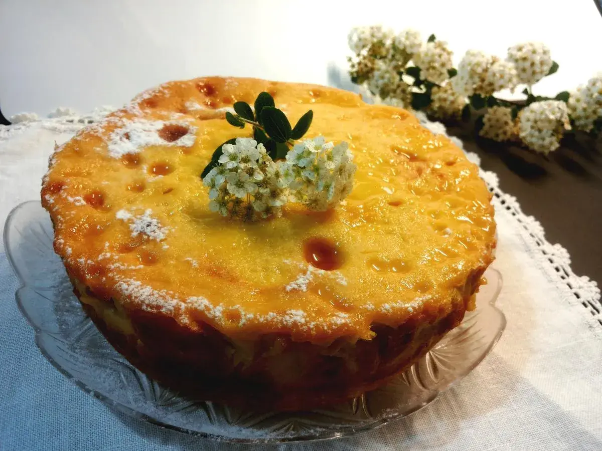 Deliziosa torta di riso massese, dorata e lucida, decorata con fiori bianchi e spolverata di zucchero a velo.