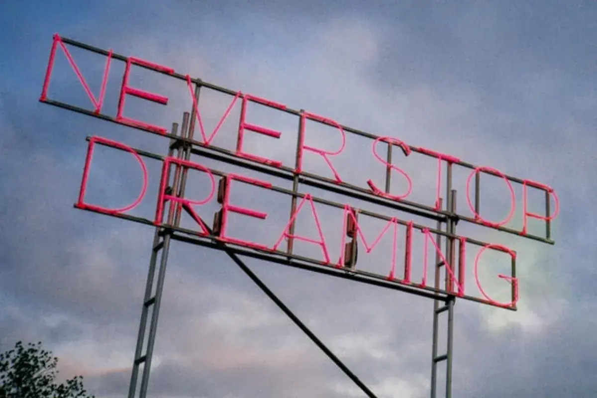 Insegna al neon rosa con la scritta "NEVER STOP DREAMING". Un promemoria ispiratore, come frasi sulla rinascita in inglese, per non smettere mai di sognare.