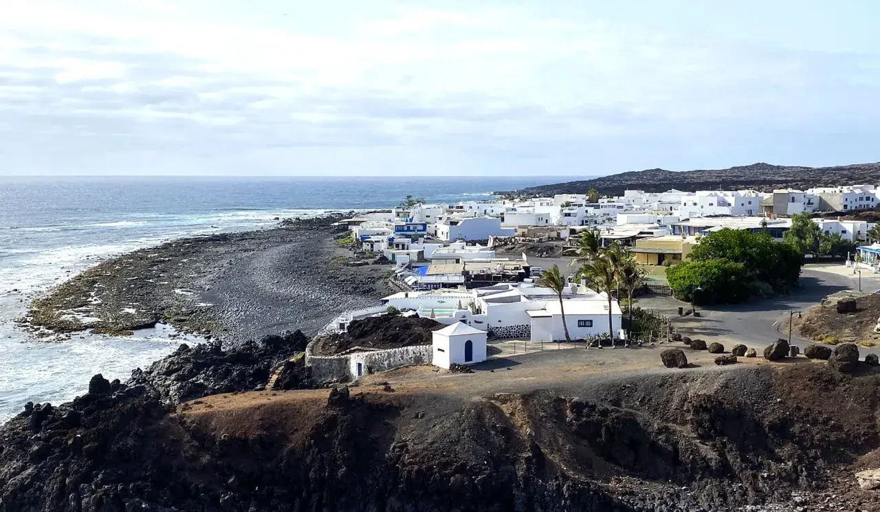 Pueblo blanco costero con mar azul y rocas volcánicas. Un ejemplo de las cosas que ver en Lanzarote.