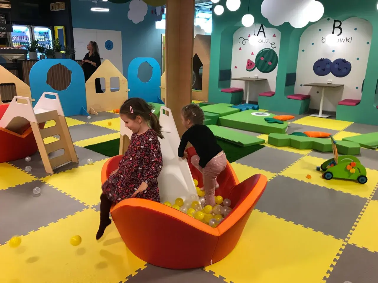 Dwie dziewczynki bawią się w sali zabaw Smart Kids Planet Warszawa. Jedna zjeżdża po zjeżdżalni do basenu z piłeczkami.