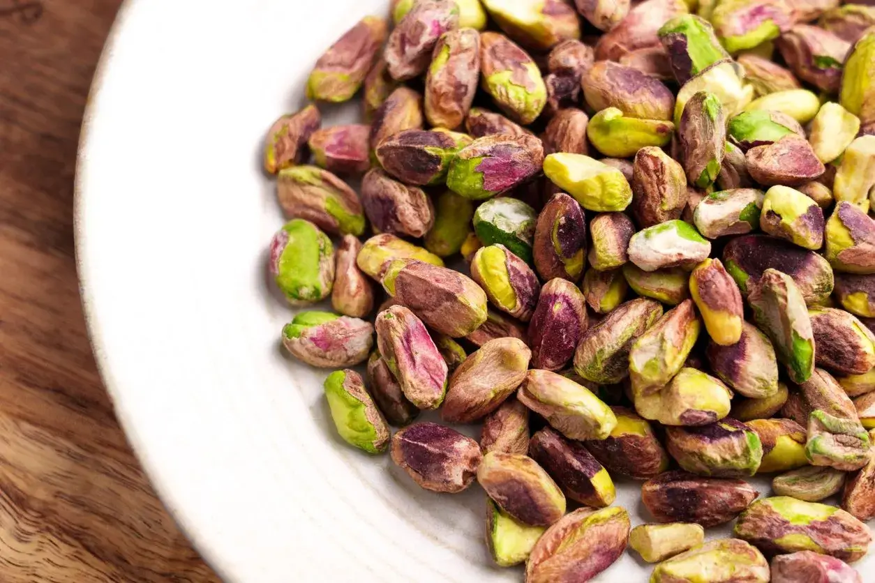 Pistacchi sgusciati su un piatto bianco, un assaggio di dove cresce il pistacchio in Italia, con i loro colori verdi e viola.