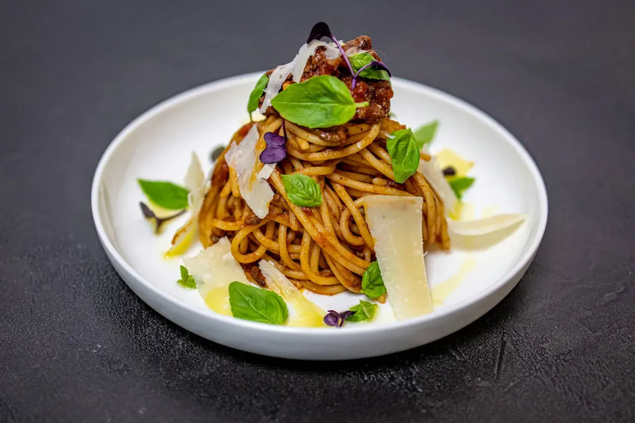 Pyszne spaghetti alla norma z sosem pomidorowym, bakłażanem, bazylią i parmezanem, podane na białym talerzu.