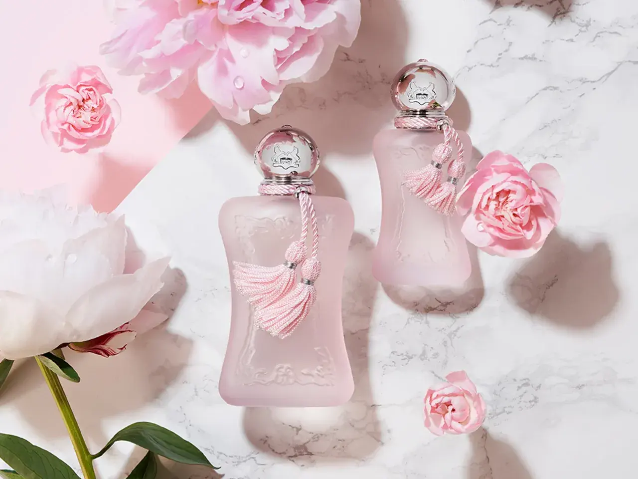 Dwa różowe flakoniki perfum de marly delina otoczone delikatnymi różowymi kwiatami i piwoniami.