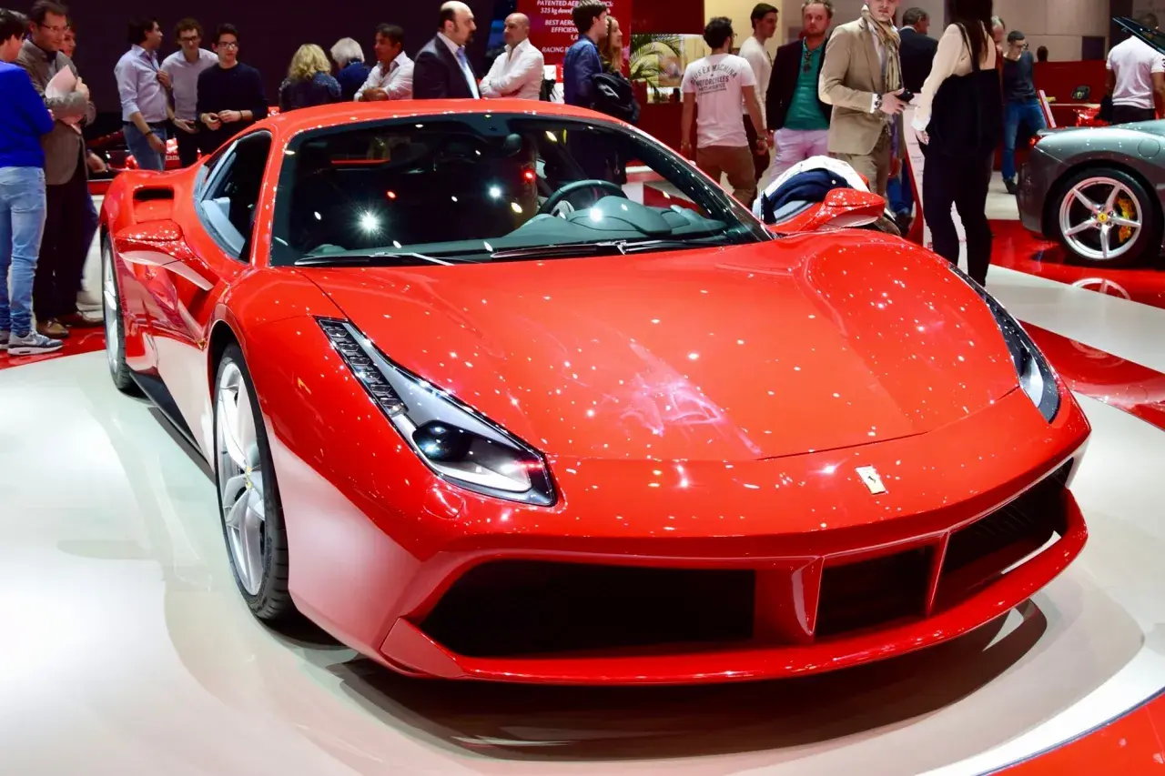 Błyszczący, czerwony Ferrari 488 GTB na wystawie, otoczony ludźmi podziwiającymi jego sportowy design.