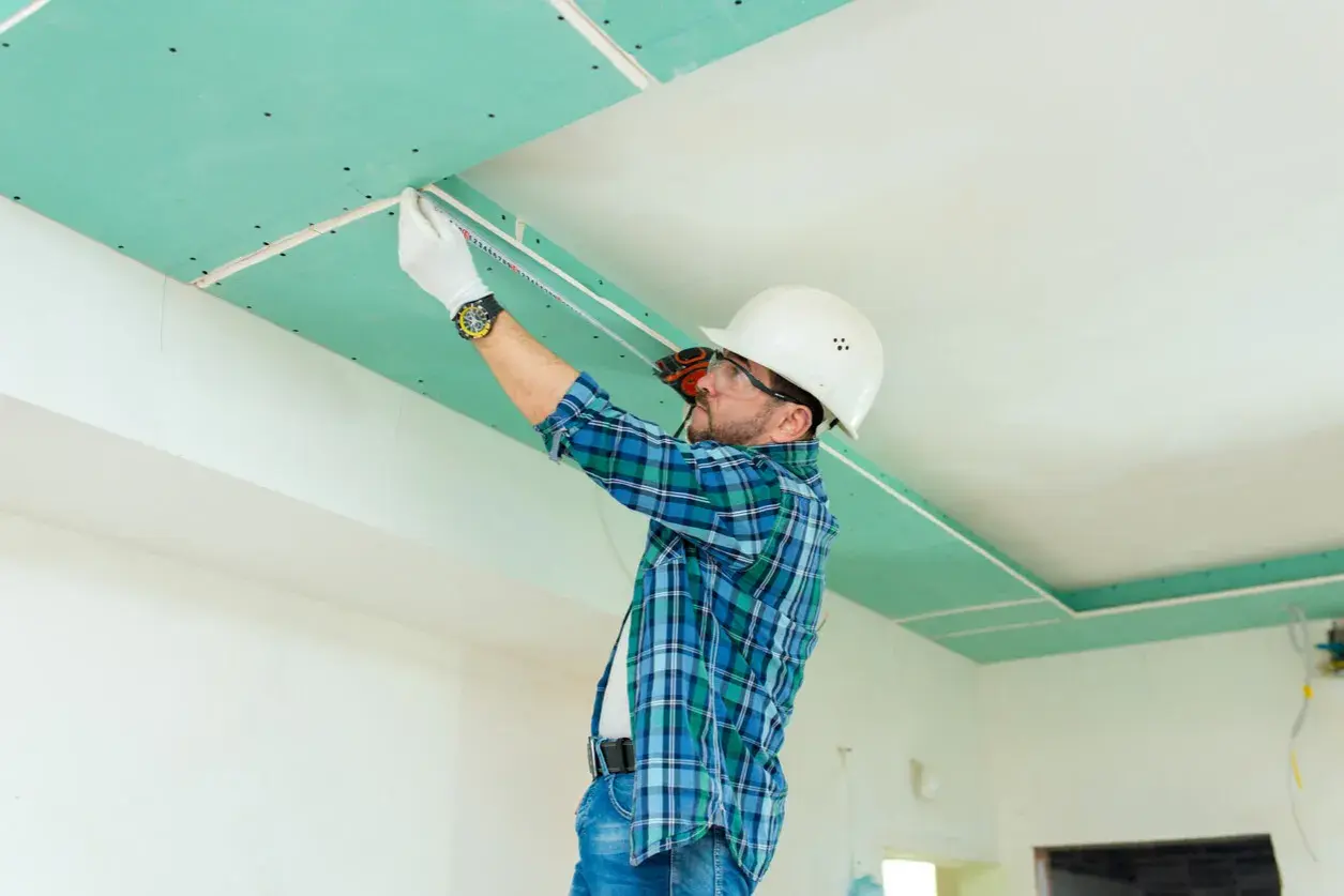Operaio con casco misura il soffitto in cartongesso, pronto per lo stucco.