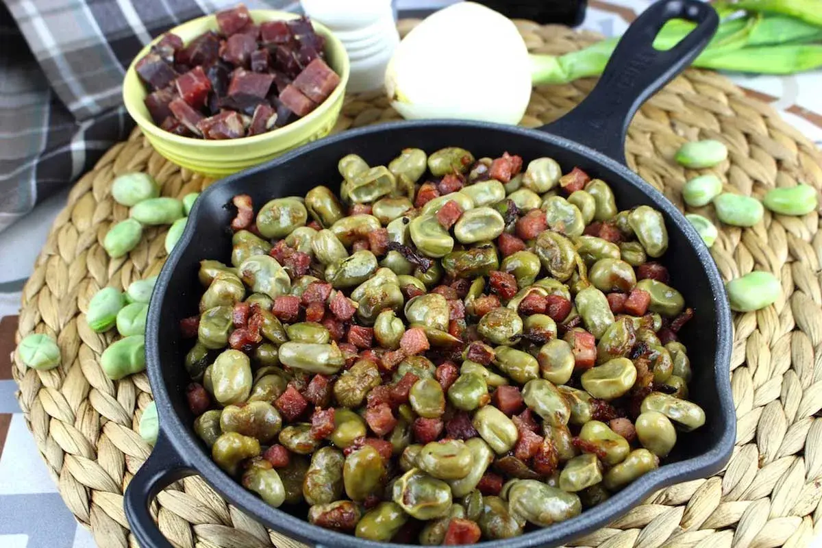 Habas tiernas salteadas con trocitos de jamón en una sartén de hierro fundido, un plato tradicional lleno de sabor.