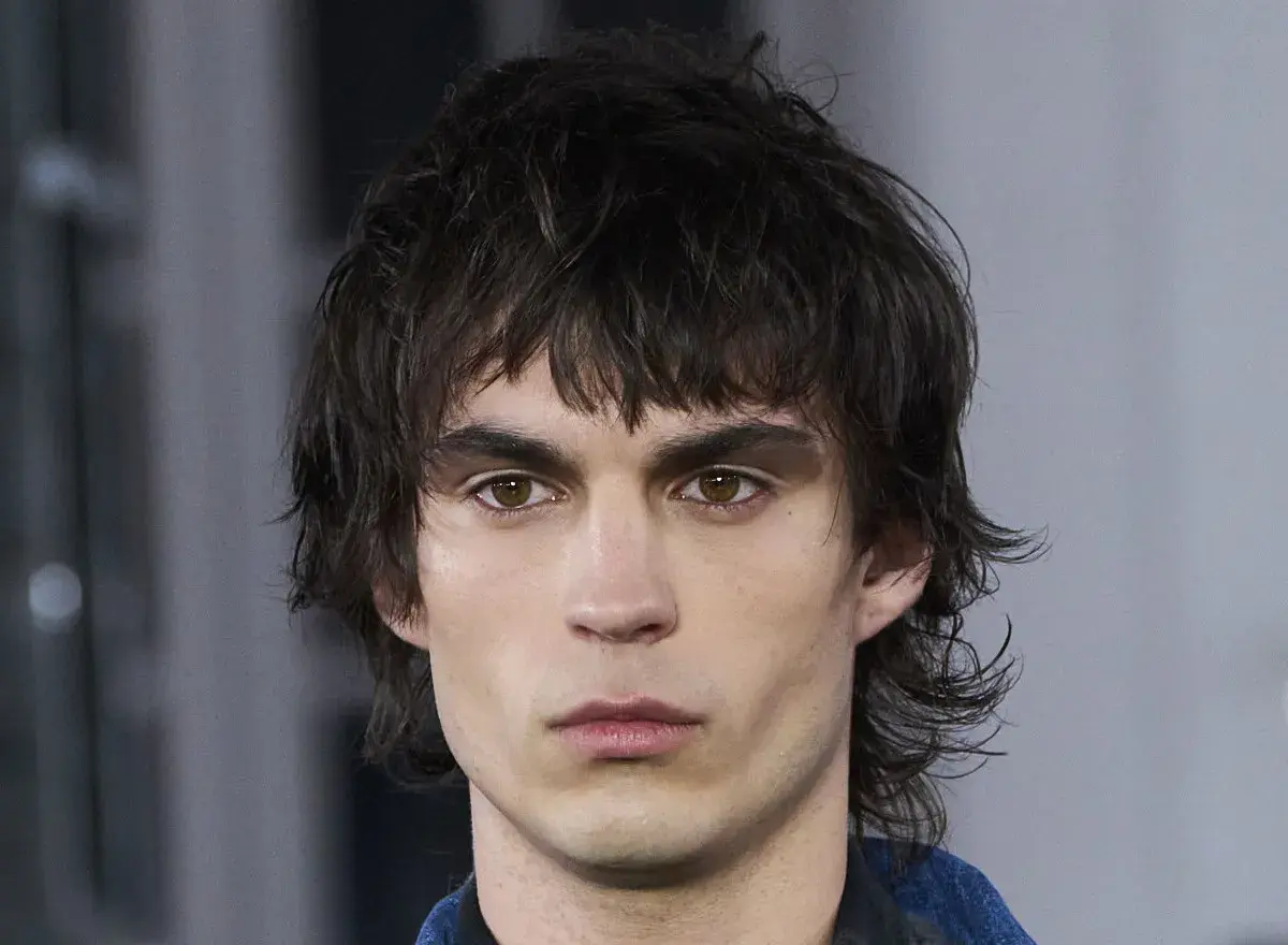 Hombre con un moderno mullet de pelo corto, mirada intensa y cejas marcadas.