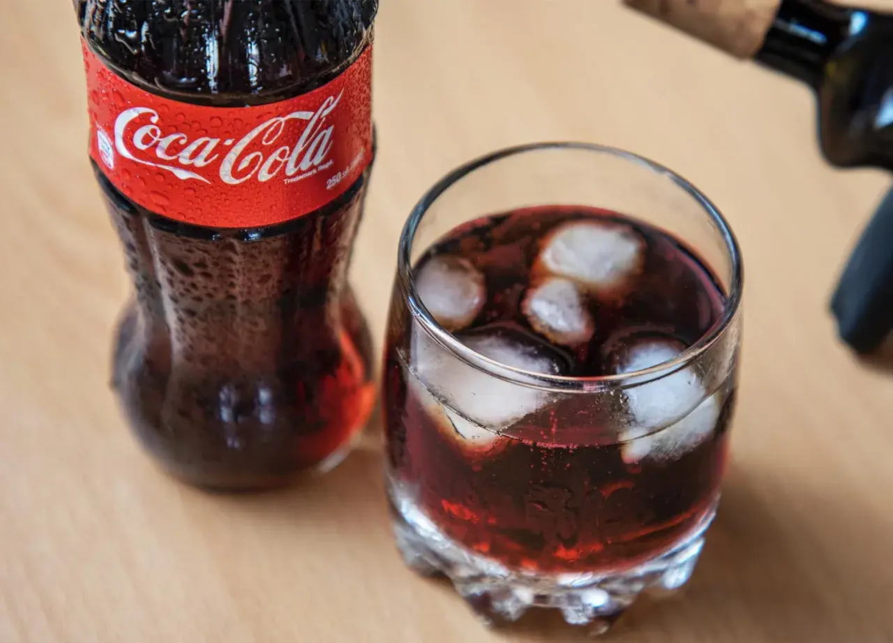 Szklanka z lodem i napojem, obok butelka Coca-Coli. Czerwone wino z colą w szklance, orzeźwiające.
