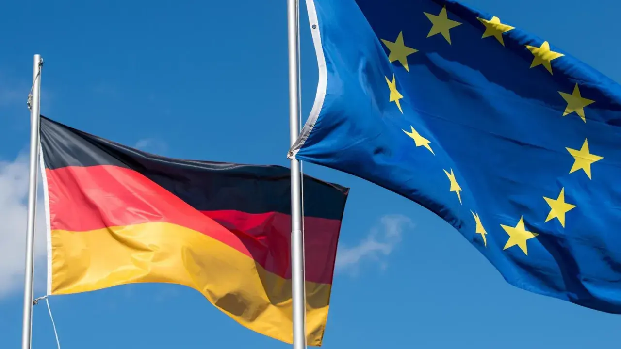 Die deutsche und die EU-Flagge wehen im Wind vor blauem Himmel.