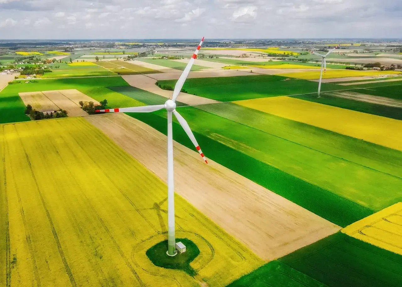 Wiatrak na tle pól rzepaku i zbóż. Nowa ustawa wiatrakowa wspiera takie inwestycje w zieloną energię.