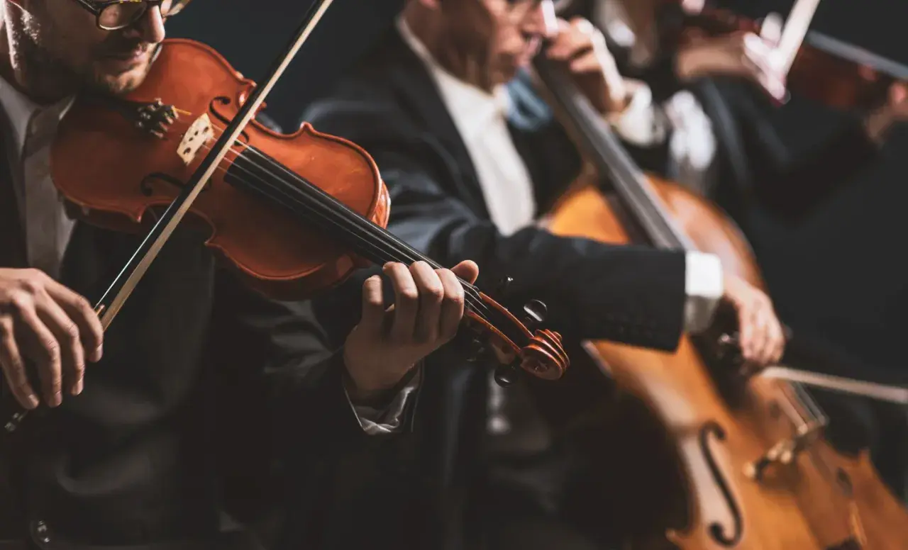 Muzycy w eleganckich strojach grają na instrumentach smyczkowych. W centrum uwagi skrzypek, a w tle wiolonczela. To piękny intro do koncertu.