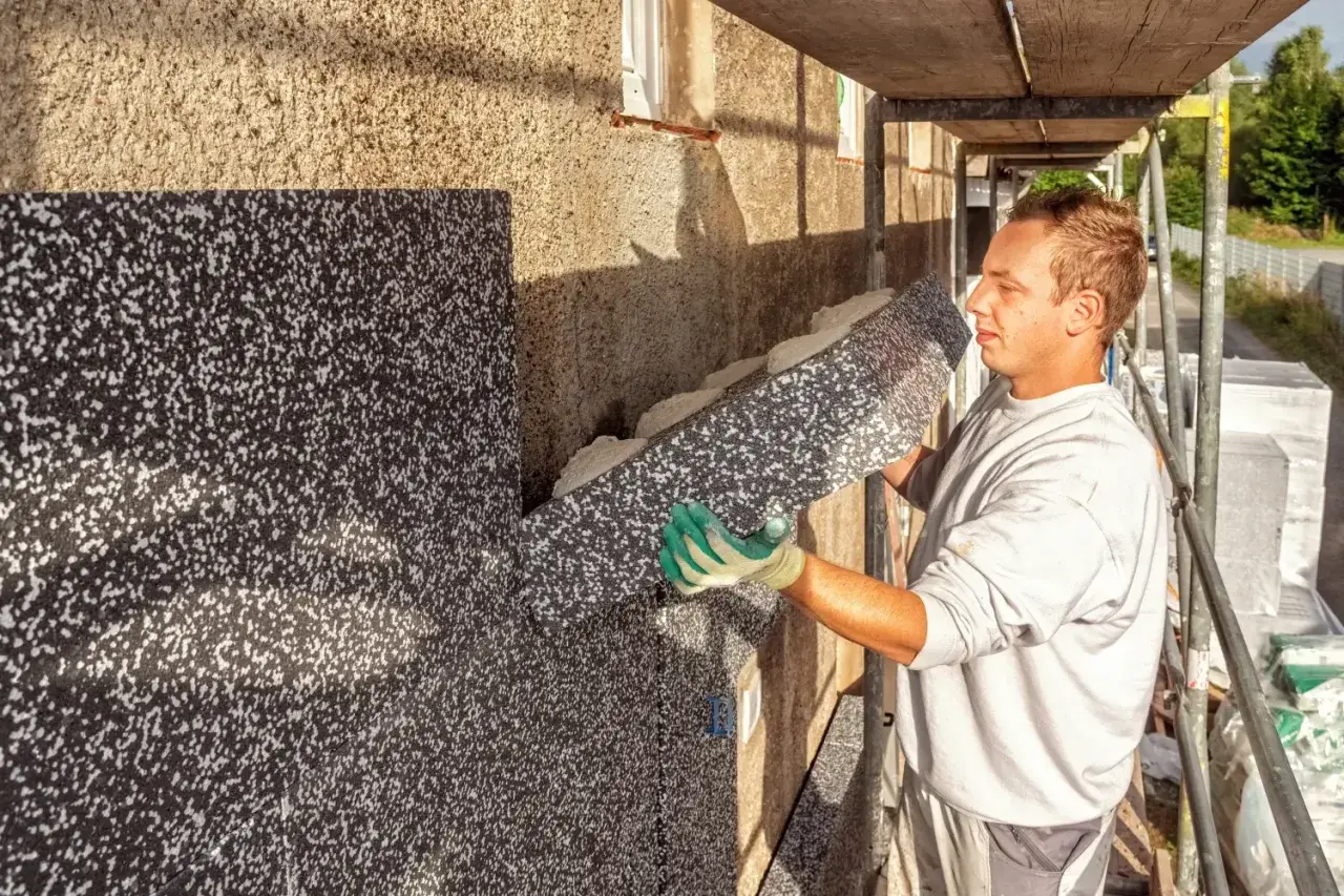 Pracownik montuje styropian na ścianie starego domu, zapobiegając wilgoci i poprawiając izolację.