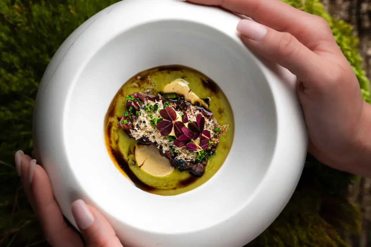 Wykwintne danie z restauracji z gwiazdką Michelin, podane w białej misie na tle mchu.