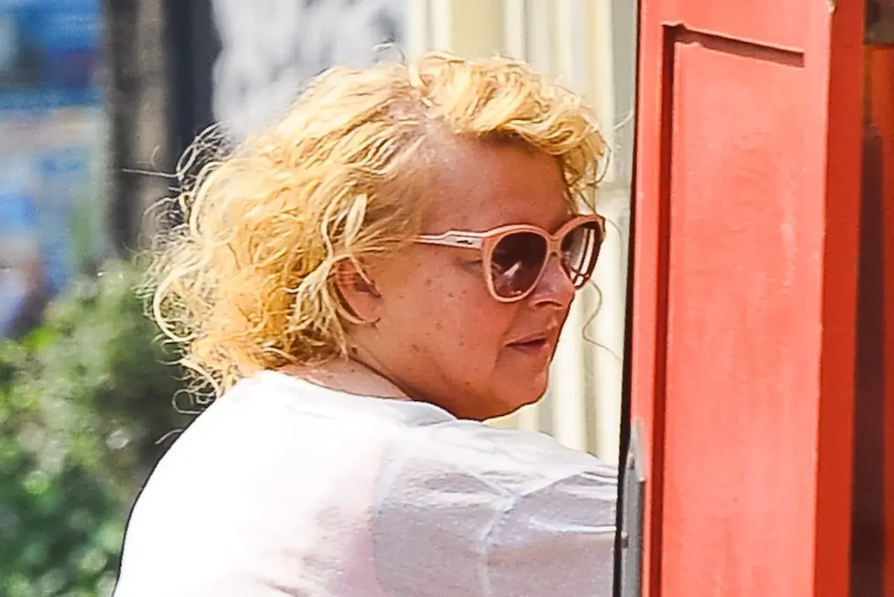 Magda Gessler bez peruki, w okularach przeciwsłonecznych, z kręconymi blond włosami, w białej koszulce.