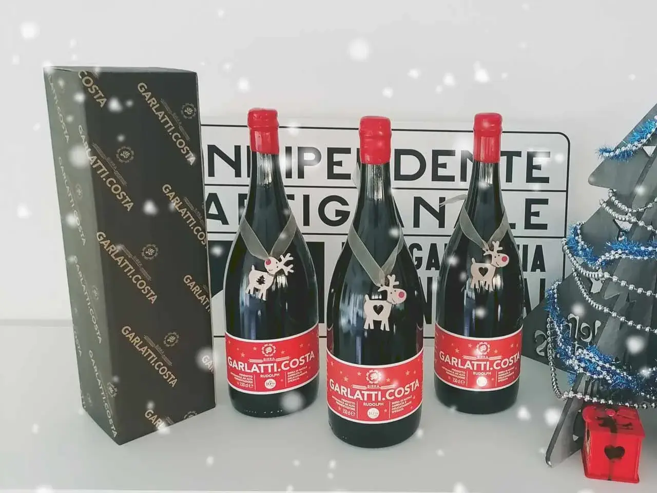 Tre bottiglie di birra Garlatti.Costa con decorazioni natalizie, una scatola e un albero di Natale sullo sfondo.