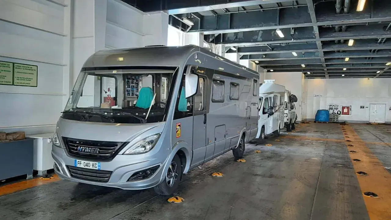 Camping-cars alignés dans la cale d'un ferry, prêts pour la traversée vers la Corse. Le tarif de la traversée pour la Corse en camping-car est affiché sur un panneau.