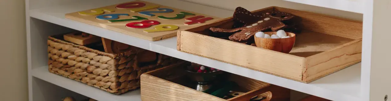 Drewniane pudło na zabawki z pluszowym piernikiem i kuleczkami. Obok puzzle z cyframi i wiklinowy kosz.