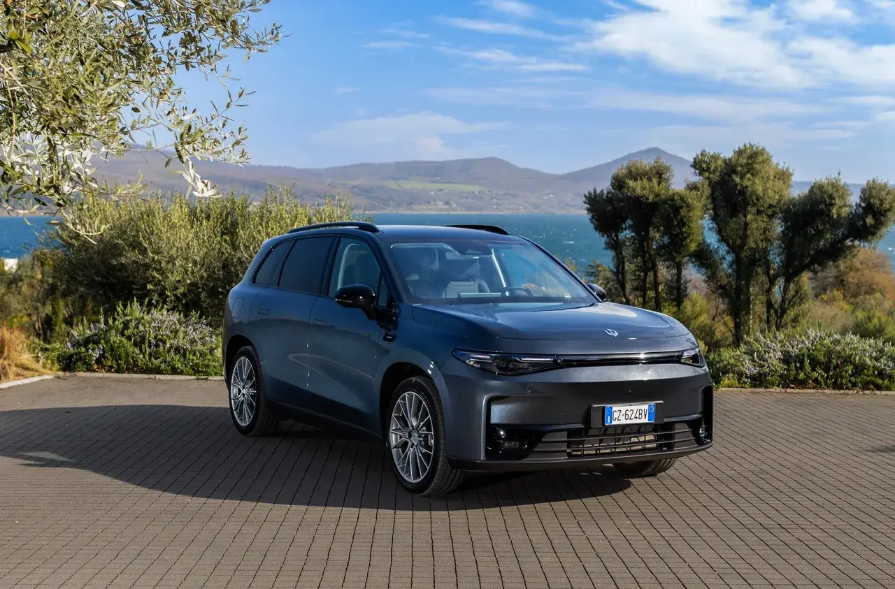 Leapmotor B10 REEV, un SUV elettrico dal design moderno, parcheggiato su un selciato con vista su un lago e colline verdi.