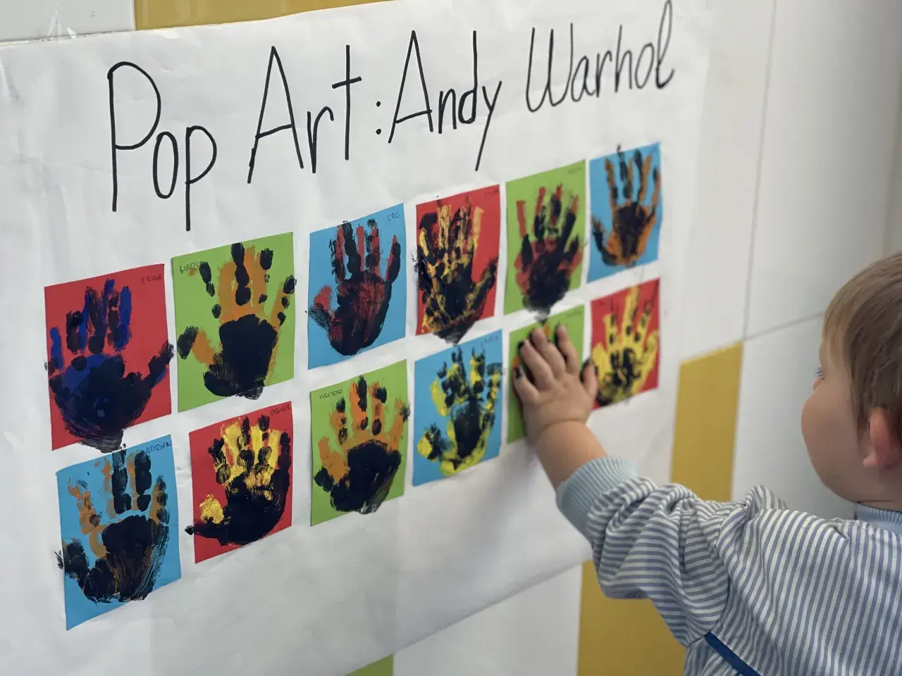 Manos pequeñas crean arte pop inspirado en Andy Warhol. Un niño toca una obra colorida, celebrando la creatividad infantil.