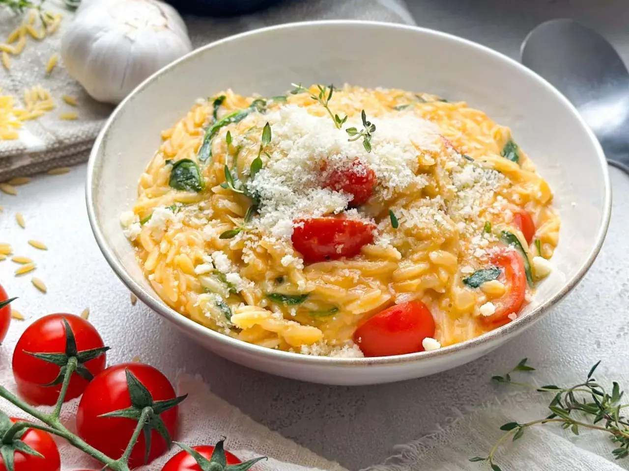 Schüssel mit Orzotto, Tomaten, Spinat und Parmesan, garniert mit Thymian.