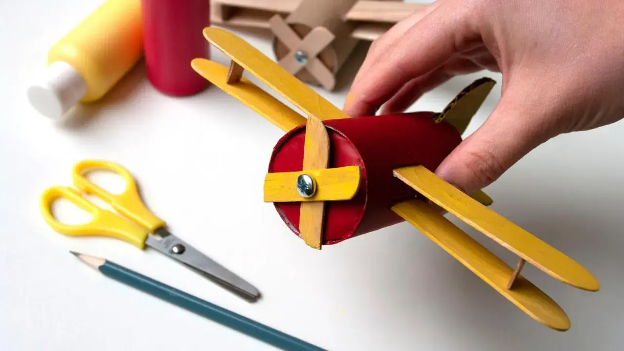 Un avión hecho con materiales de **avión manualidades**, sostenido por una mano. Tijeras y lápiz cerca, listos para crear más.
