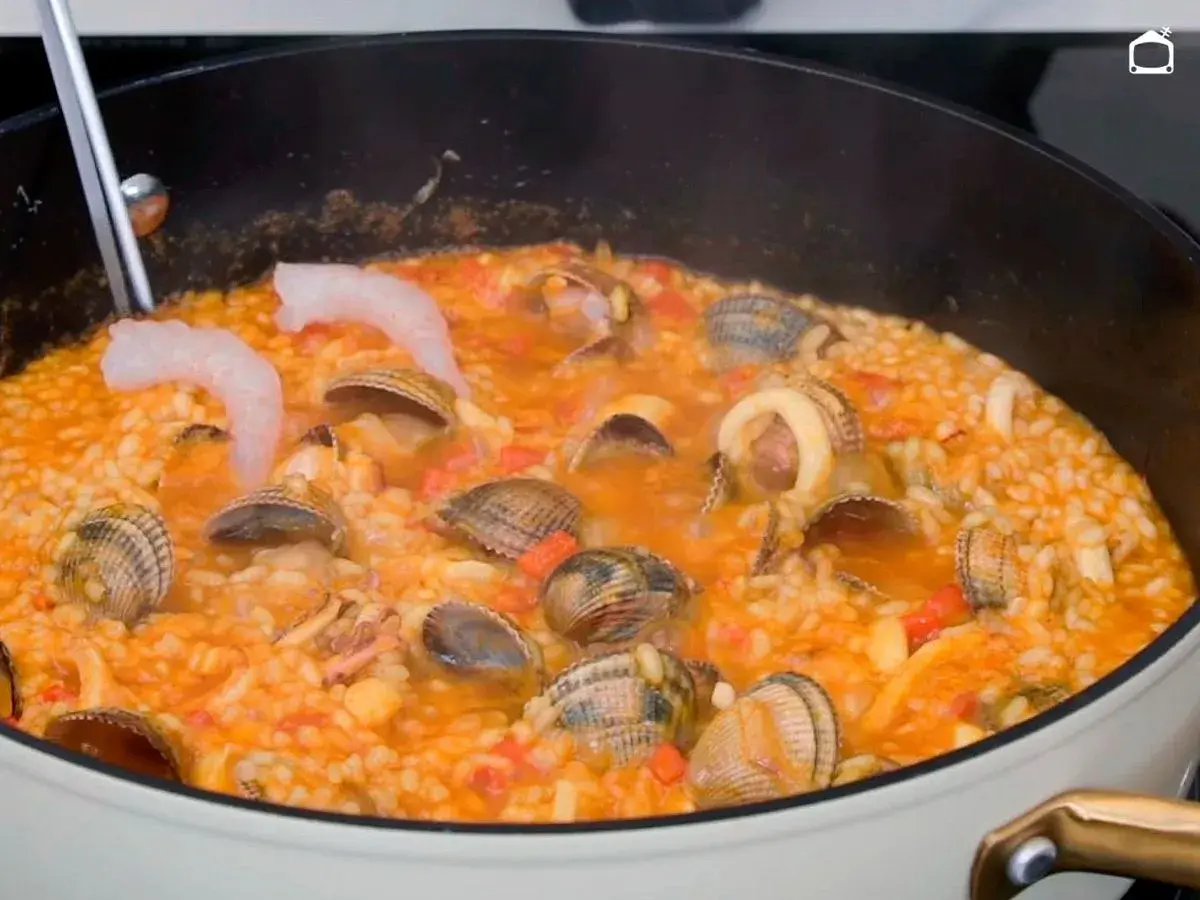 Un delicioso arroz a la marinera burbujea en una sartén, con gambas, almejas y calamares.