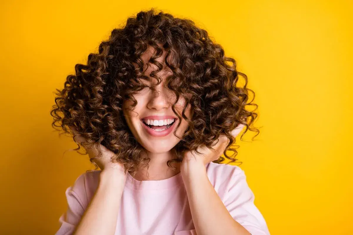 Mujer sonríe con cabello rizado y voluminoso. Descubre cómo hidratar el cabello después de una permanente para mantenerlo así de saludable.