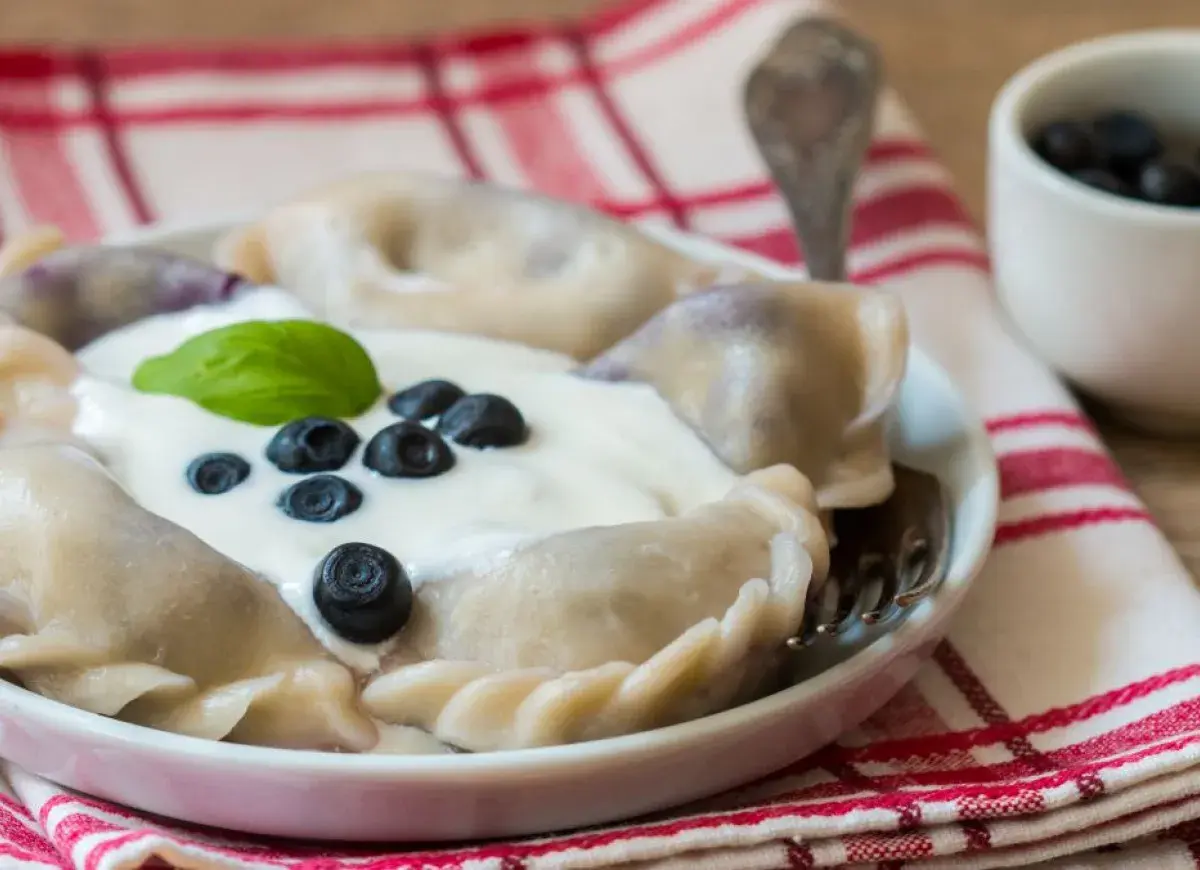 Pyszne pierogi z borówkami amerykańskimi, polane śmietaną i ozdobione świeżymi owocami. Idealne na letni deser.
