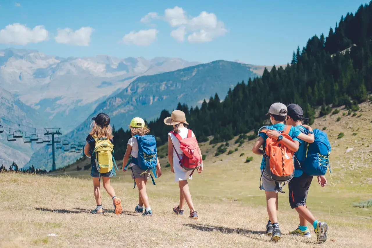 Niños explorando los Pirineos con mochilas, disfrutando de un día soleado con vistas a las montañas y un telesilla.